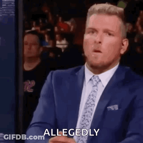 A Man In A Suit And Tie Is Sitting In Front Of A Crowd . GIF