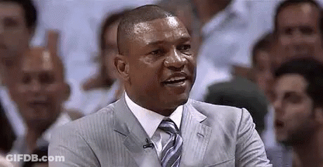 A Man In A Suit And Tie Is Sitting In Front Of A Crowd Of People . GIF