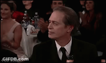 A Man In A Suit And Tie Is Sitting In Front Of A Crowd Of People Clapping . GIF