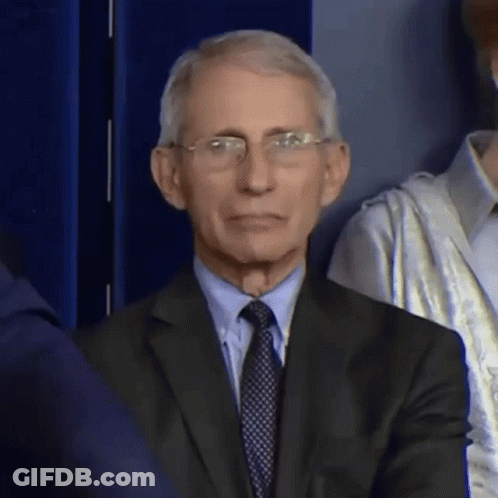 A Man In A Suit And Tie Is Sitting In Front Of A Crowd . GIF