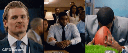 A Man In A Suit And Tie Is Sitting In Front Of A Group Of People GIF