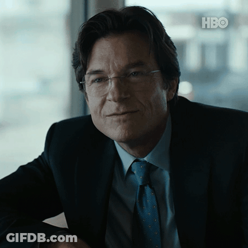A Man In A Suit And Tie Is Sitting In Front Of A Hbo Logo GIF
