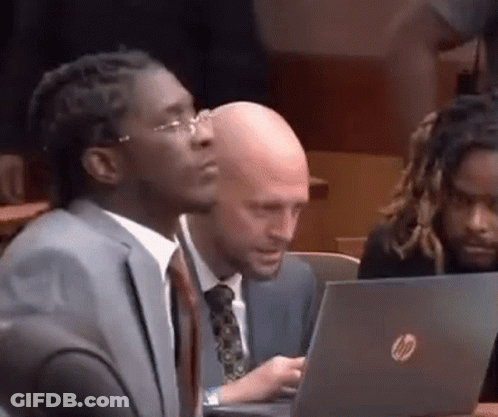 A Man In A Suit And Tie Is Sitting In Front Of A Laptop . GIF