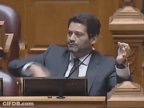 A Man In A Suit And Tie Is Sitting In Front Of A Microphone GIF