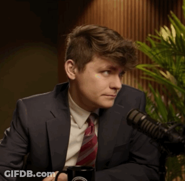 A Man In A Suit And Tie Is Sitting In Front Of A Microphone And Holding A Mug That Says ' Washington ' GIF