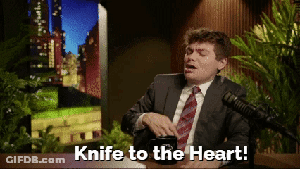 A Man In A Suit And Tie Is Sitting In Front Of A Microphone And Says Knife To The Heart GIF