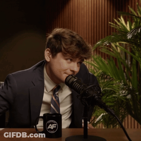 A Man In A Suit And Tie Is Sitting In Front Of A Microphone With A Black Mug That Says Af On It GIF
