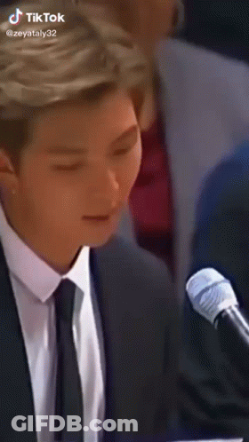 A Man In A Suit And Tie Is Sitting In Front Of A Microphone With His Eyes Closed . GIF