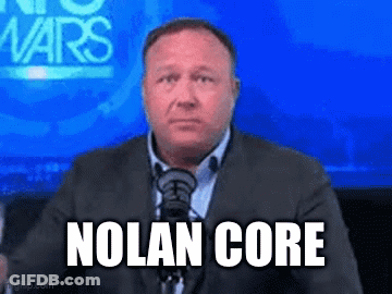 A Man In A Suit And Tie Is Sitting In Front Of A Microphone With The Words Nolan Core On His Face GIF