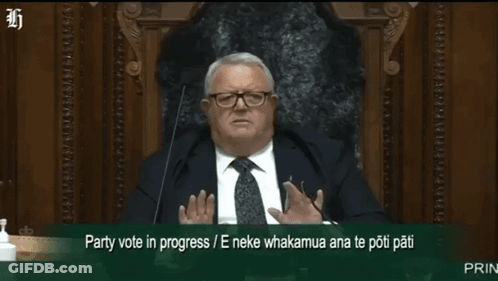 A Man In A Suit And Tie Is Sitting In Front Of A Microphone With The Words Party Vote In Progress Written Below Him GIF