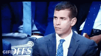 A Man In A Suit And Tie Is Sitting In Front Of A Offs Sign GIF