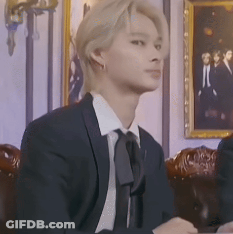 A Man In A Suit And Tie Is Sitting In Front Of A Picture On The Wall . GIF
