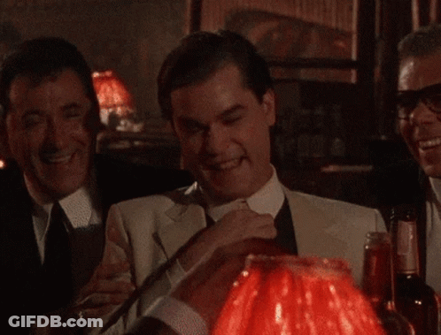A Man In A Suit And Tie Is Sitting In Front Of A Red Lamp GIF