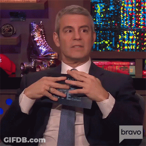 Man In Suit And Tie Sitting In Front Of Bravo Sign GIF