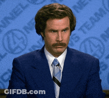 A Man In A Suit And Tie Is Sitting In Front Of A Sign That Says ' News Team ' GIF