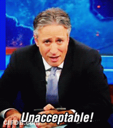 A Man In A Suit And Tie Is Sitting In Front Of A Sign That Says Unacceptable GIF