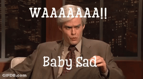 A Man In A Suit And Tie Is Sitting In Front Of A Sign That Says Waaaaaaa Baby Sad GIF