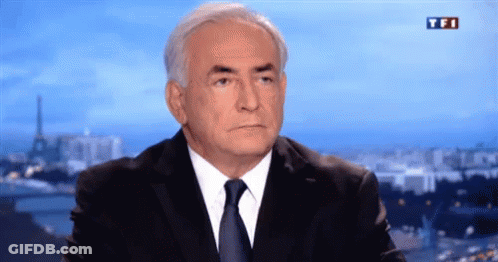 A Man In A Suit And Tie Is Sitting In Front Of A TV Screen That Says Tfi GIF