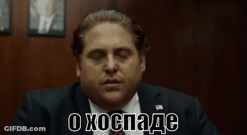 A Man In A Suit And Tie Is Sitting In Front Of A Wall With His Eyes Closed And Making A Funny Face . GIF