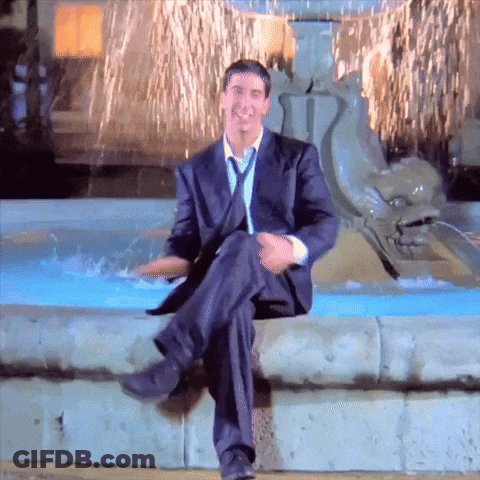 A Man In A Suit And Tie Is Sitting In Front Of A Water Fountain GIF