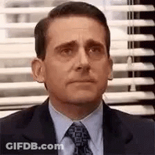 A Man In A Suit And Tie Is Sitting In Front Of A Window . GIF