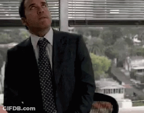 A Man In A Suit And Tie Is Sitting In Front Of A Window And Looking Up . GIF