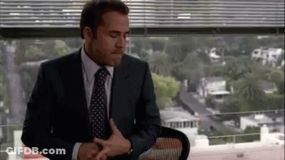 A Man In A Suit And Tie Is Sitting In Front Of A Window In An Office . GIF