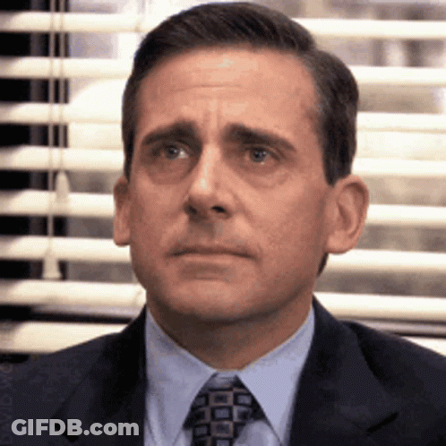 A Man In A Suit And Tie Is Sitting In Front Of A Window GIF