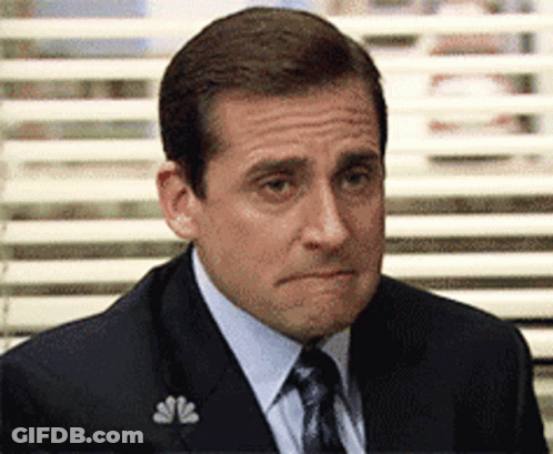 A Man In A Suit And Tie Is Sitting In Front Of A Window With Blinds . GIF
