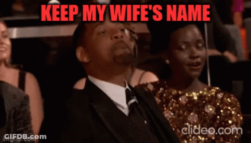 A Man In A Suit And Tie Is Sitting In Front Of A Woman With The Words Keep My Wife 'S Name Above Him GIF