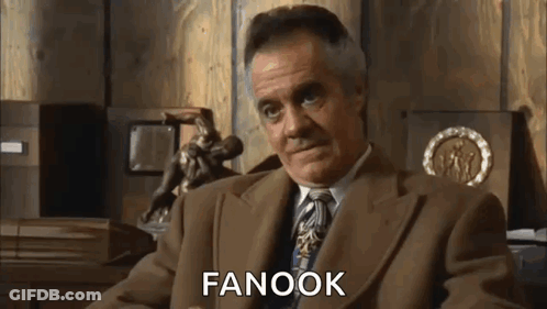 A Man In A Suit And Tie Is Sitting In Front Of A Wooden Wall And Talking . GIF