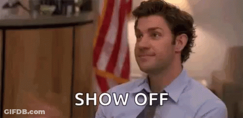 A Man In A Suit And Tie Is Sitting In Front Of An American Flag And Says `` Show Off '' . GIF