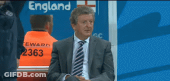 A Man In A Suit And Tie Is Sitting In Front Of An England Sign GIF