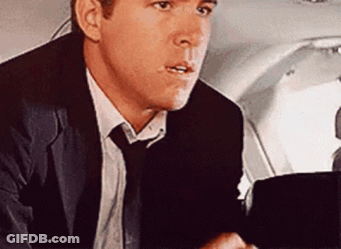 A Man In A Suit And Tie Is Sitting In The Back Seat Of A Plane . GIF