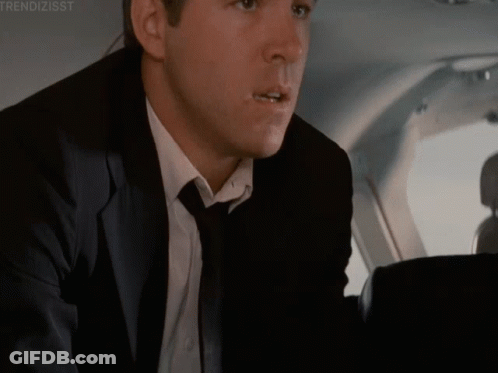 A Man In A Suit And Tie Is Sitting In The Back Seat Of A Plane GIF