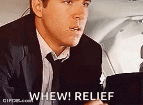 A Man In A Suit And Tie Is Sitting In The Back Seat Of An Airplane And Says `` Whew ! Relief '' . GIF