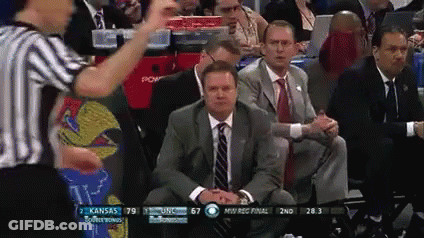 A Man In A Suit And Tie Is Sitting In The Stands Watching A Basketball Game Between Kansas And Usc GIF