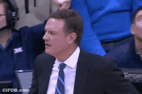 A Man In A Suit And Tie Is Sitting In The Stands Watching A Game GIF