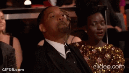A Man In A Suit And Tie Is Sitting Next To A Woman In A Gold Dress GIF