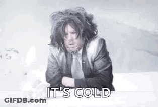 A Man In A Suit And Tie Is Sitting On A Bed With His Arms Crossed And Says `` It 'S Cold '' . GIF
