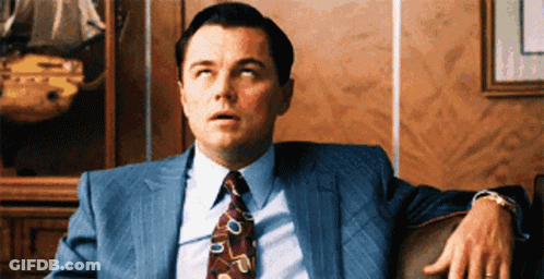 A Man In A Suit And Tie Is Sitting On A Chair GIF