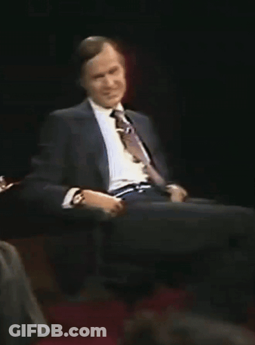 A Man In A Suit And Tie Is Sitting On A Chair GIF