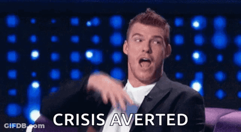 A Man In A Suit And Tie Is Sitting On A Couch And Making A Funny Face While Saying Crisis Averted GIF