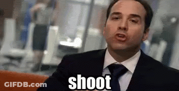 A Man In A Suit And Tie Is Sitting On A Couch And Says Shoot . GIF