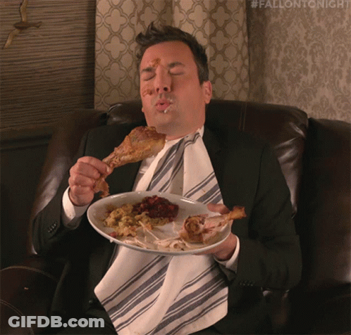 A Man In A Suit And Tie Is Sitting On A Couch Eating Chicken GIF