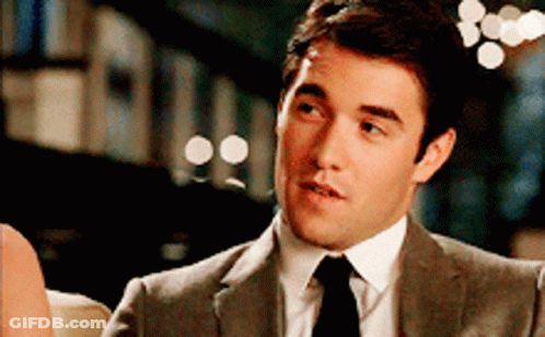 A Man In A Suit And Tie Is Sitting On A Couch Talking To Another Man . GIF