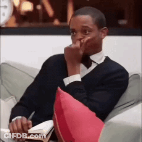 A Man In A Suit And Tie Is Sitting On A Couch With A Book And A Pen In His Hand . GIF