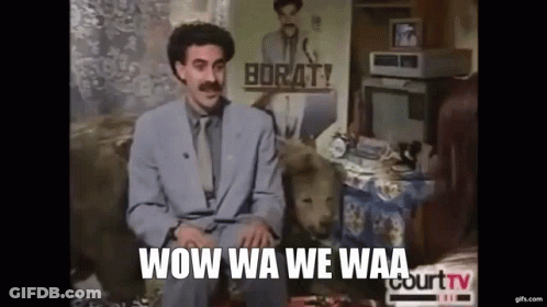 A Man In A Suit And Tie Is Sitting On A Couch With A Dog In Front Of Him . GIF