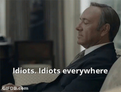 A Man In A Suit And Tie Is Sitting On A Couch With His Eyes Closed And The Words Idiots Idiots Everywhere Below Him GIF