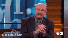A Man In A Suit And Tie Is Sitting On A Couch With His Hands Folded GIF